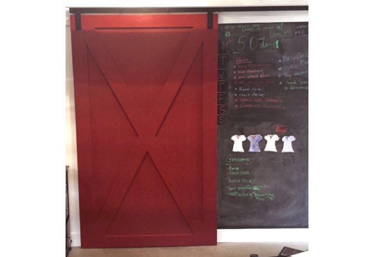 Red x-frame sliding barn door with black hardware next to chalkboard 